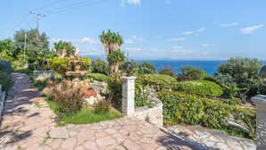 A garden pathway leading to a statue, with a view of the sea and lush greenery. - Apartment 'Stefanos Place Sea View' with Sea View, Wi-Fi and Air Conditioning (Corfu)