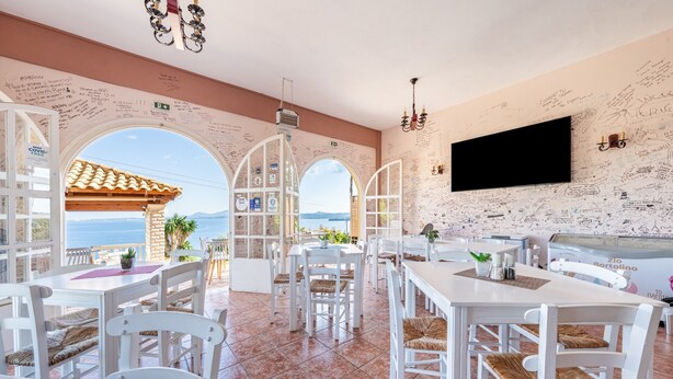 A restaurant with white furniture, a TV mounted on the wall, and handwritten notes on the walls. - Apartment 'Stefanos Place Sea View' with Sea View, Wi-Fi and Air Conditioning (Corfu)