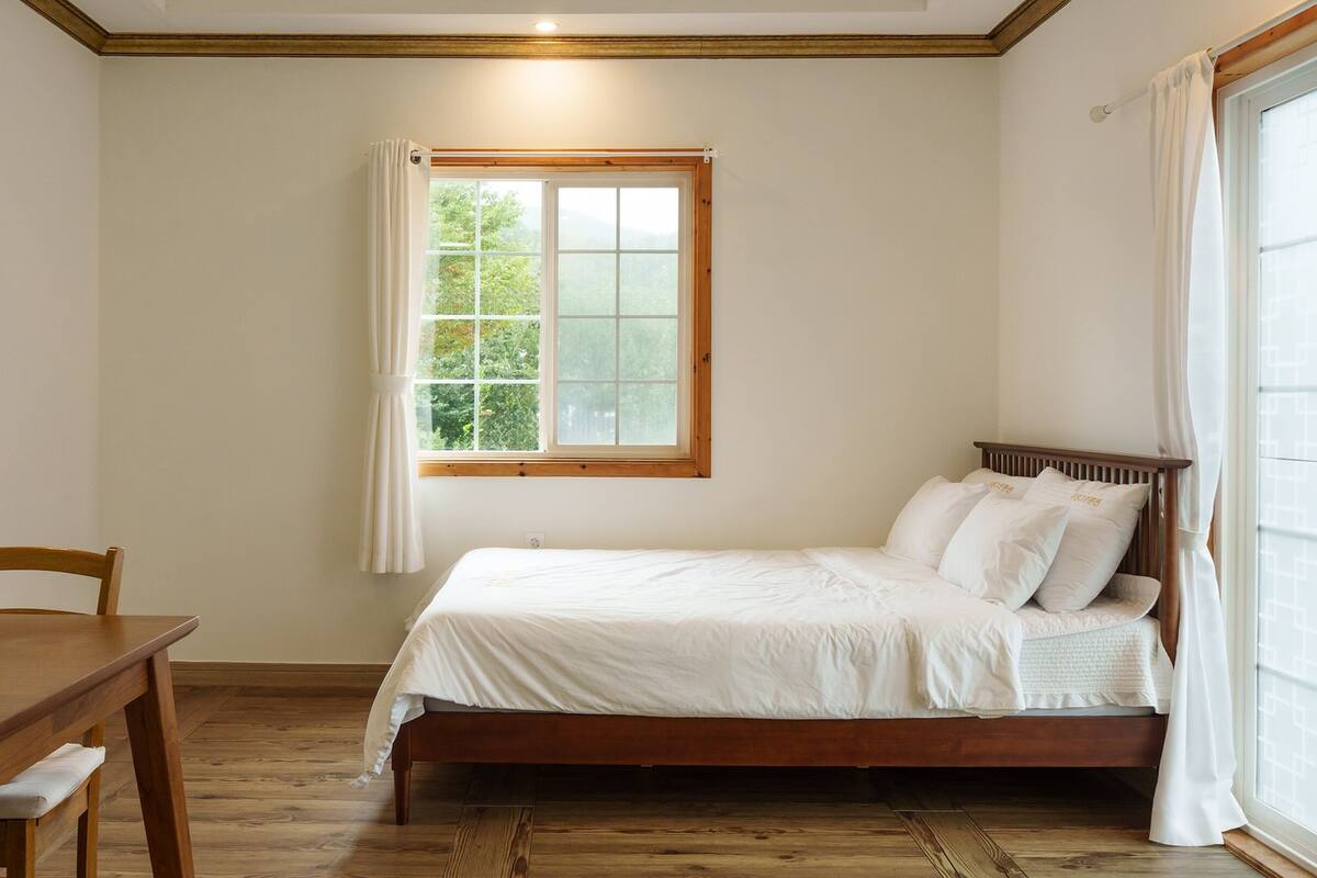 A bedroom with a wooden bed, a desk with a chair, a television, and a window with curtains.