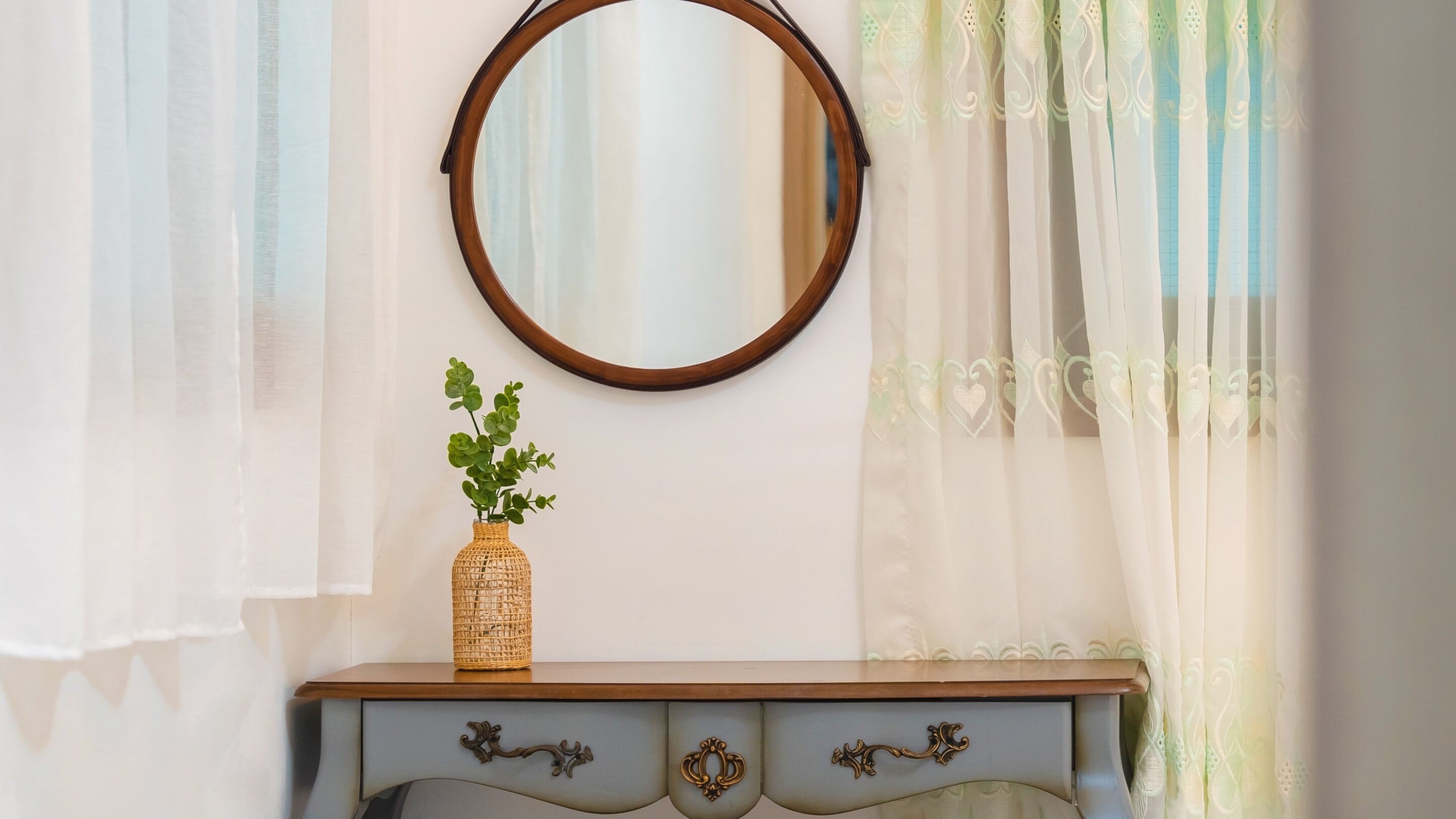 Un tocador de madera con espejo, una cesta trenzada con follaje verde y un cajón azul claro con adornos.