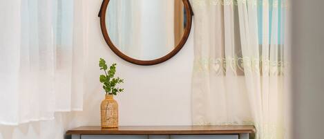 Un tocador de madera con espejo, una cesta trenzada con follaje verde y un cajón azul claro con adornos.