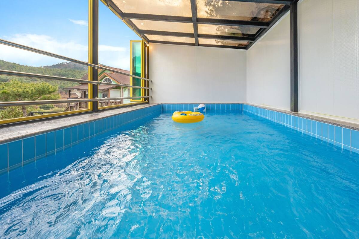 An indoor swimming pool with clear blue water, a yellow inflatable ring, and a view of a mountainous landscape through large windows.