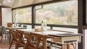 A dining area with wooden tables and chairs, a buffet station, and a view of cherry blossoms through large windows. - Gyeongju Woojin Green Pension (Gyeongju)
