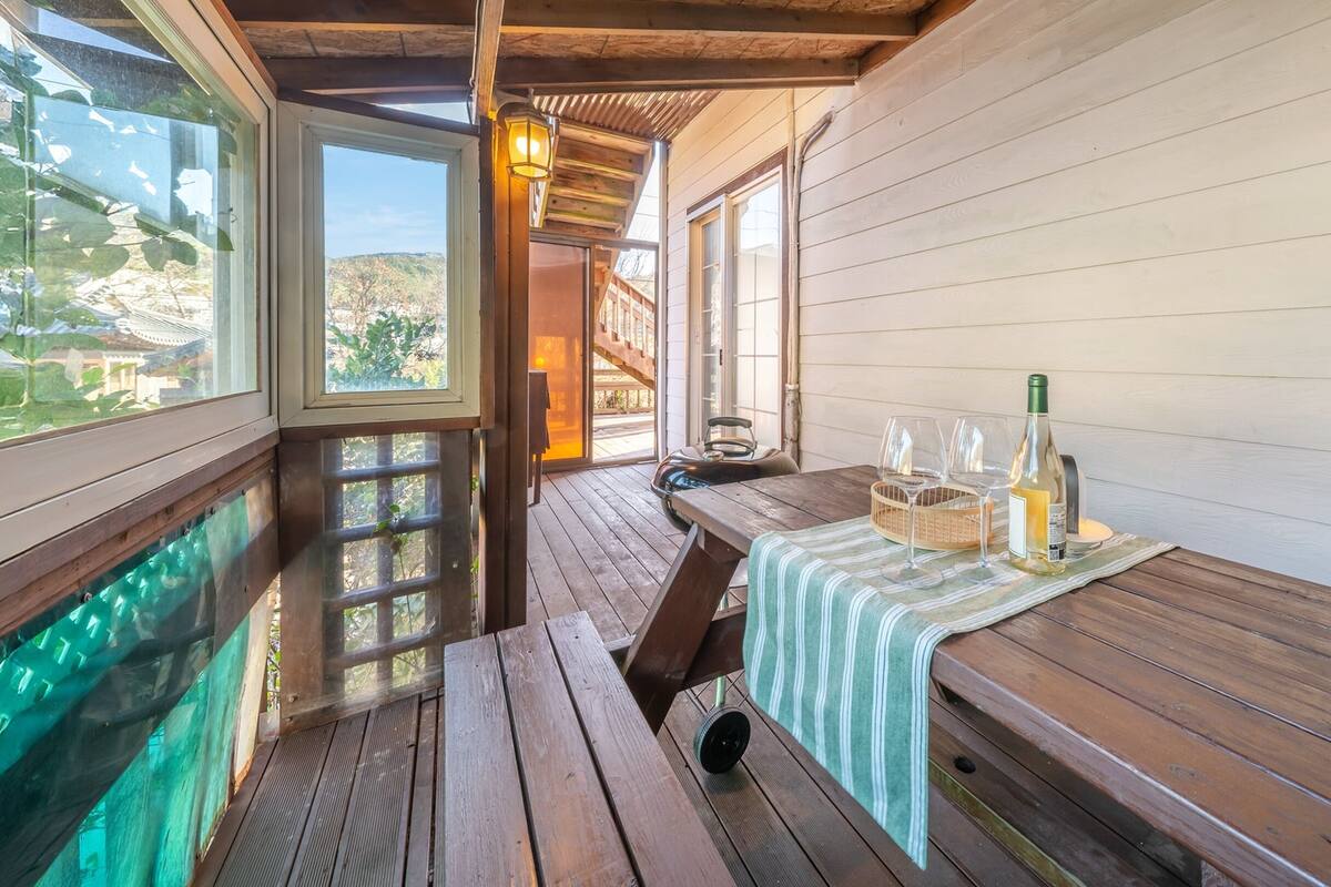 A wooden deck with a table set for dining, overlooking a pool and a mountainous landscape.