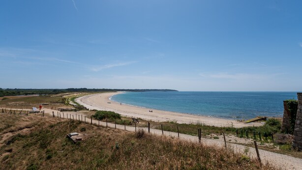 Un paysage côtier avec une plage de sable, un ciel bleu dégagé et une ligne de côte lointaine.