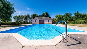 Une piscine rectangulaire avec un escalier en métal, entourée d’une terrasse en béton et avec un bâtiment visible à l’arrière-plan.