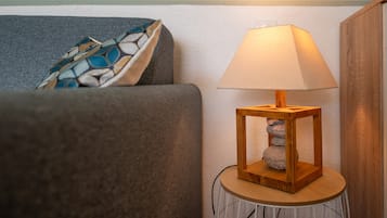 A room with a grey sofa, a patterned throw pillow, a wooden lamp on a small table, and a white cable.