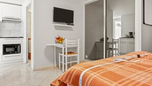 A hotel room with a bed, a TV mounted on the wall, a microwave, a small table with a fruit bowl, and a sliding door leading to a bathroom. - Studio 'L'Esterel' with Sea View, Wi-Fi, and Air Conditioning (Saint-Raphaël)