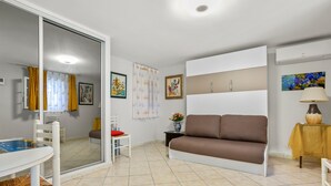 A living room with a sofa, a dining table with chairs, a sliding glass door, and a small table with a lamp. - Studio 'L'Esterel' with Sea View, Wi-Fi, and Air Conditioning (Saint-Raphaël)