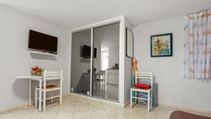 A room with a TV, two chairs, a table with fruit, a sliding door to a kitchen, and a framed picture on the wall. - Studio 'L'Esterel' with Sea View, Wi-Fi, and Air Conditioning (Saint-Raphaël)