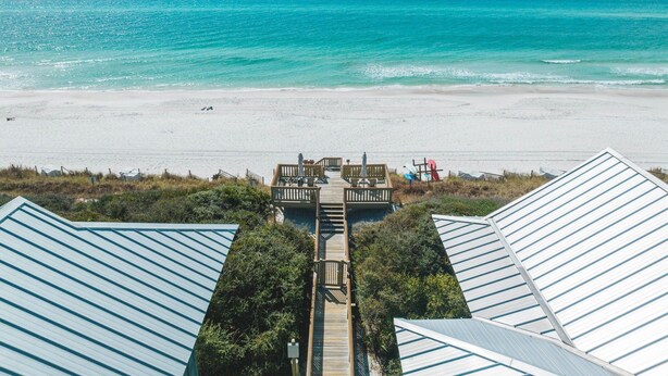 Une vue sur la plage avec une terrasse en bois menant à un bâtiment doté d’un toit en pente.