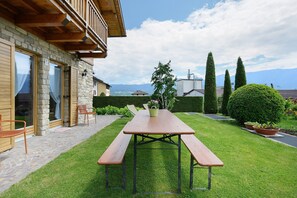 Un bâtiment en pierre doté de balcons en bois, une table de pique-nique avec des bancs, et une vue sur les montagnes.