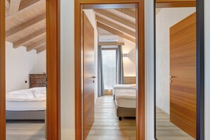 A narrow hallway with wooden floors and walls, leading to two bedrooms with wooden beds and a ceiling fan.