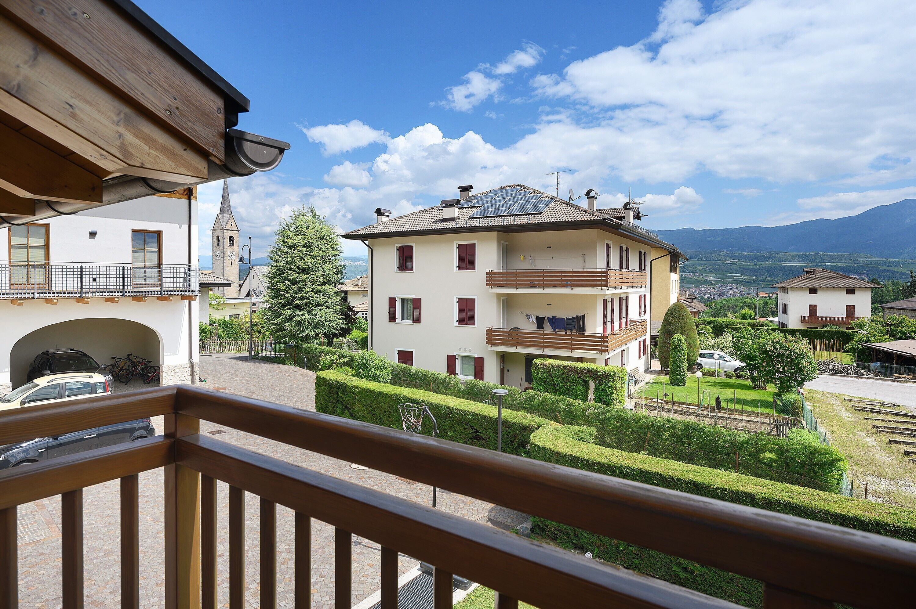 A residential building with a balcony, a church, and a mountain view.