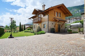 Une maison en bois à deux étages, dotée d’un balcon, d’un chemin de pierre et surplombant un paysage montagneux.