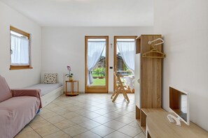 A room with a sofa, a small table with a plant, a wooden chair, a desk with a computer, and a view through a door. - Chalet 'Agritur La Crucola -' with Mountain View, Wi-Fi and Air Conditioning (Flavon)