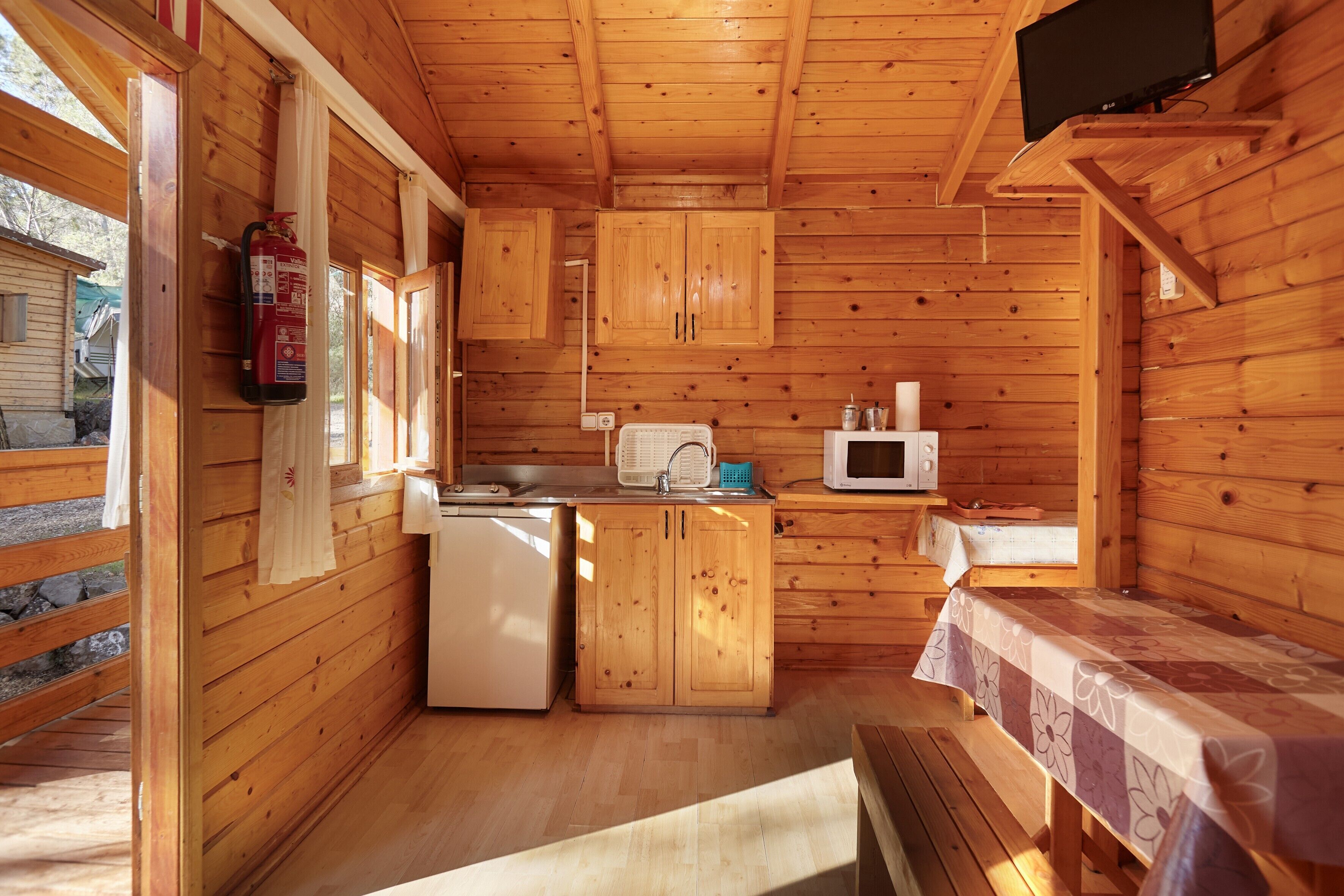 Una cabaña de madera con kitchenette, extintor, microondas y televisor.