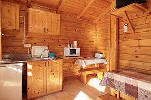 L’intérieur d’une cabane en bois comprend un coin cuisine équipé d’un réfrigérateur, d’un four à micro-ondes et de meubles de rangement en bois.