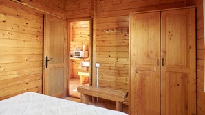A wooden cabin interior with a bed, a bench, and wooden doors.