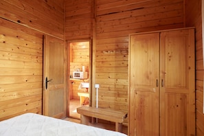 A wooden cabin interior with a bed, a bench, and wooden doors. - Country House 'Cabaña De Madera 3' with Mountain View, Shared Pool and Air Conditioning (Hornos)