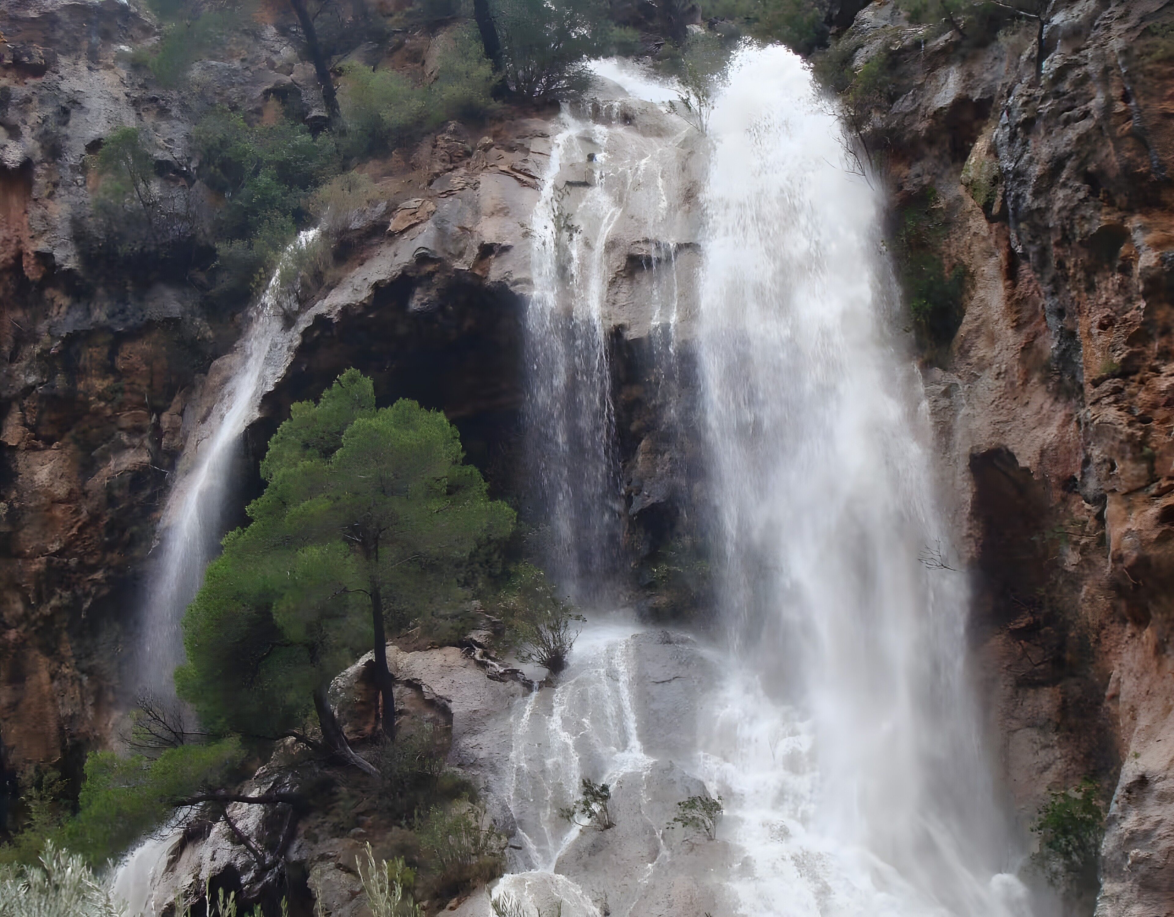Een waterval stort neer over een rotsachtige klif, omringd door groen.