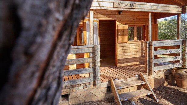 A wooden cabin with a porch, a sign reading 'La Tavola,' and a stone foundation.