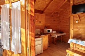 L’intérieur d’un chalet en bois comprend un coin cuisine, une table à manger recouverte d’une nappe à pois et un téléviseur fixé au mur.