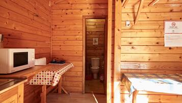 A wooden cabin interior with a kitchen area, a dining table, and a bathroom visible through an open door.