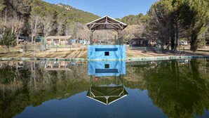 On peut clairement voir un lac avec une structure flottante, entouré d’arbres et d’un paysage vallonné.
