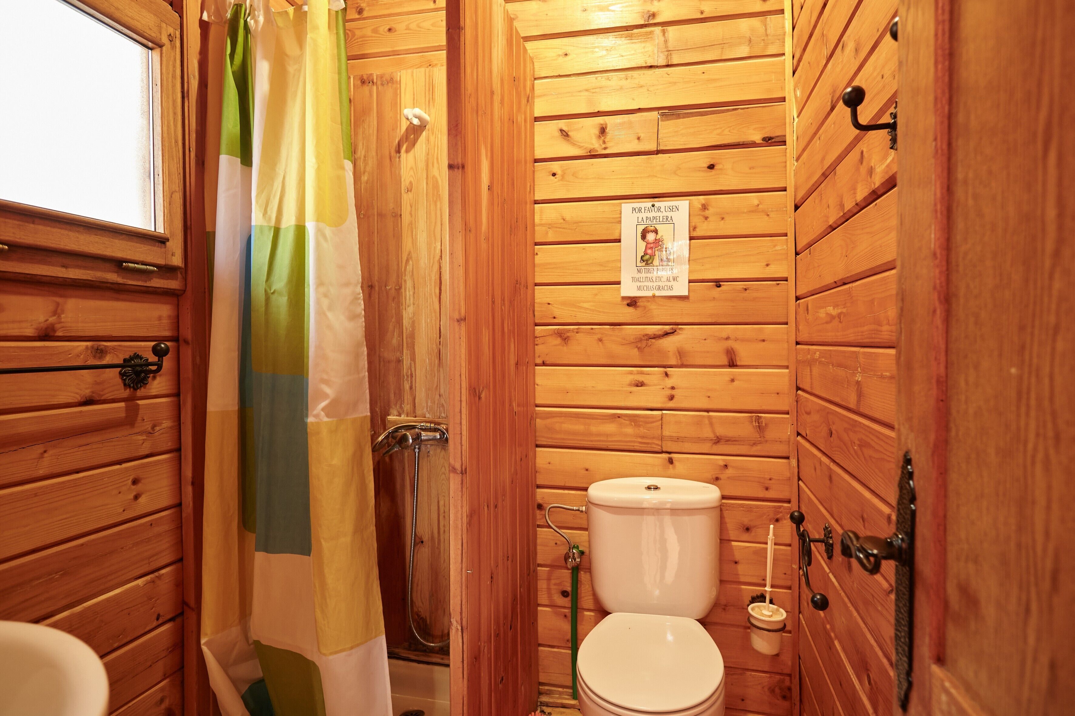 Un baño de madera con ducha, inodoro y ventana.