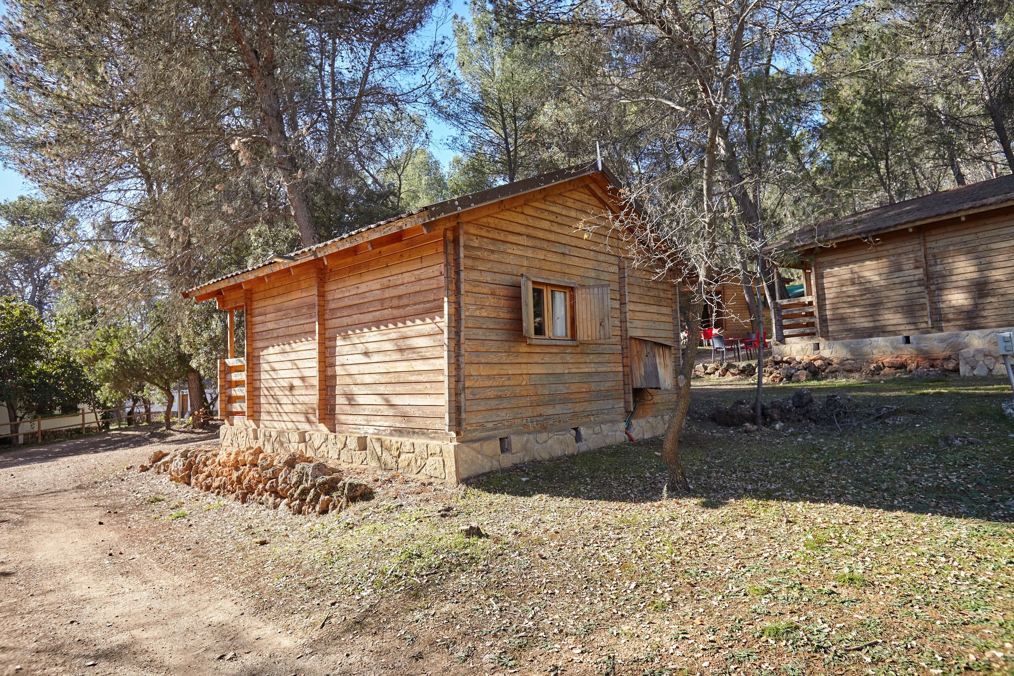Una cabaña de madera con base de piedra, un ventanal pequeño y una escalera que lleva a un porche.