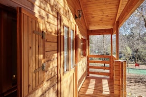 Une cabane en bois dotée d’une véranda, de grandes fenêtres et offrant une vue sur la forêt environnante.