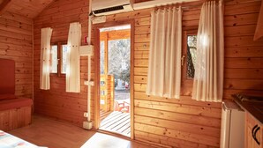 L’intérieur d’une cabane en bois comprend un lit, une table, un réfrigérateur et une porte donnant sur l’extérieur.