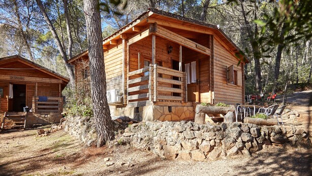 Een rustieke houten chalet met een stenen fundering en een veranda met stoelen.