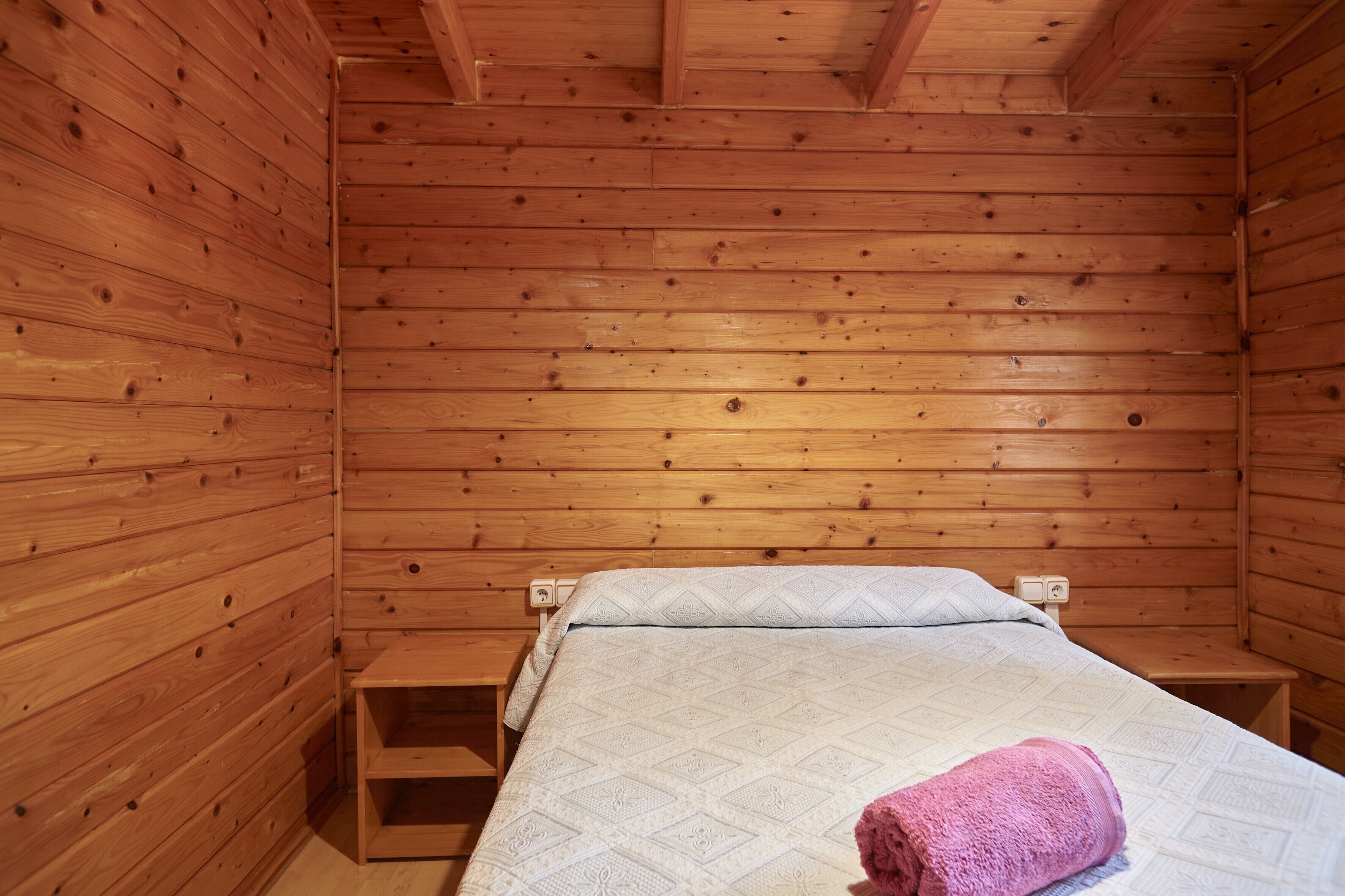 Ein Zimmer in einer Holzhütte mit einem Bett, einem Nachttisch und einem kleinen Holzschemel.