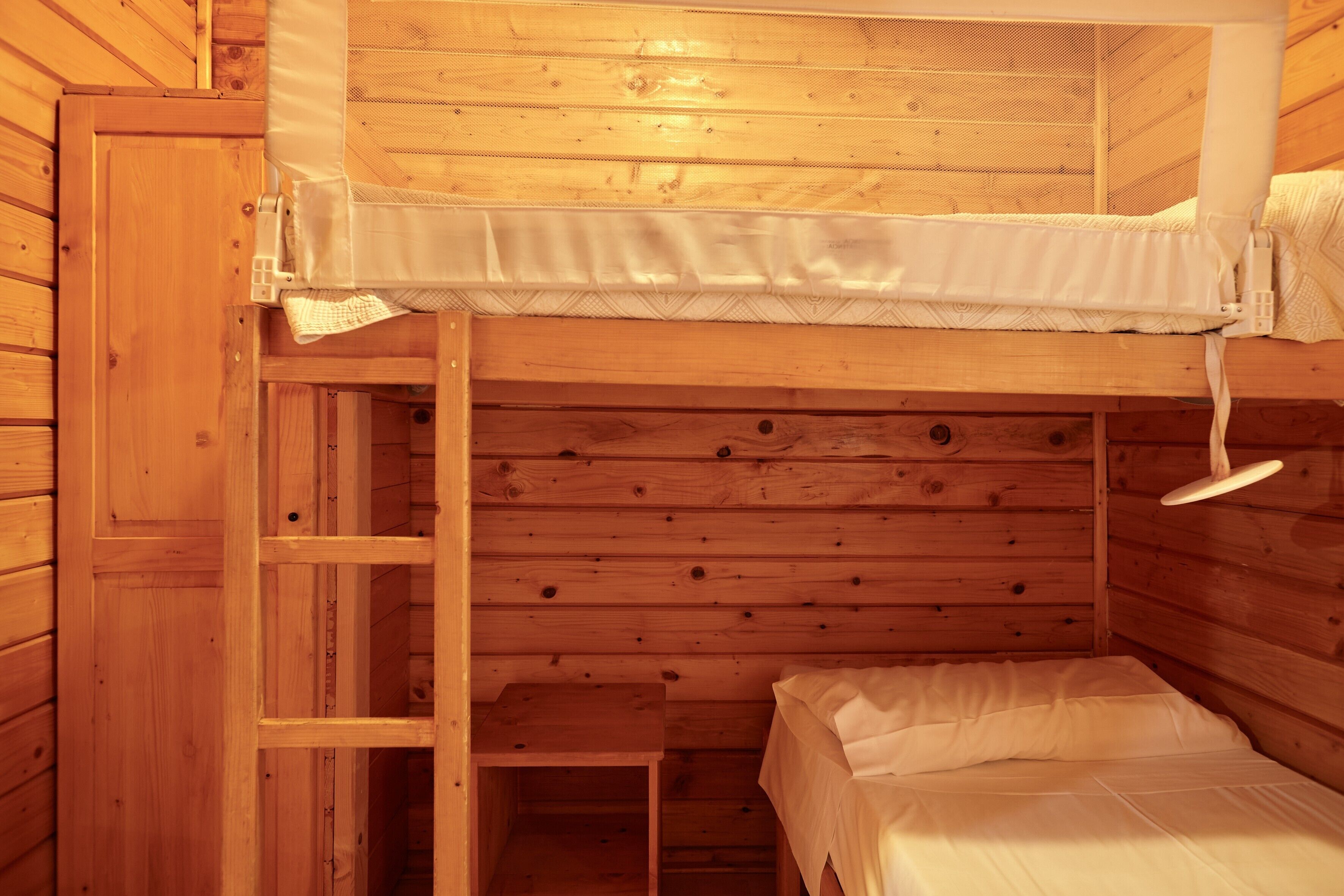 Un lit superposé avec une échelle, des murs en bois et une petite table.