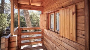 Een houten chalet met balkon, grote ramen en uitzicht op bomen.