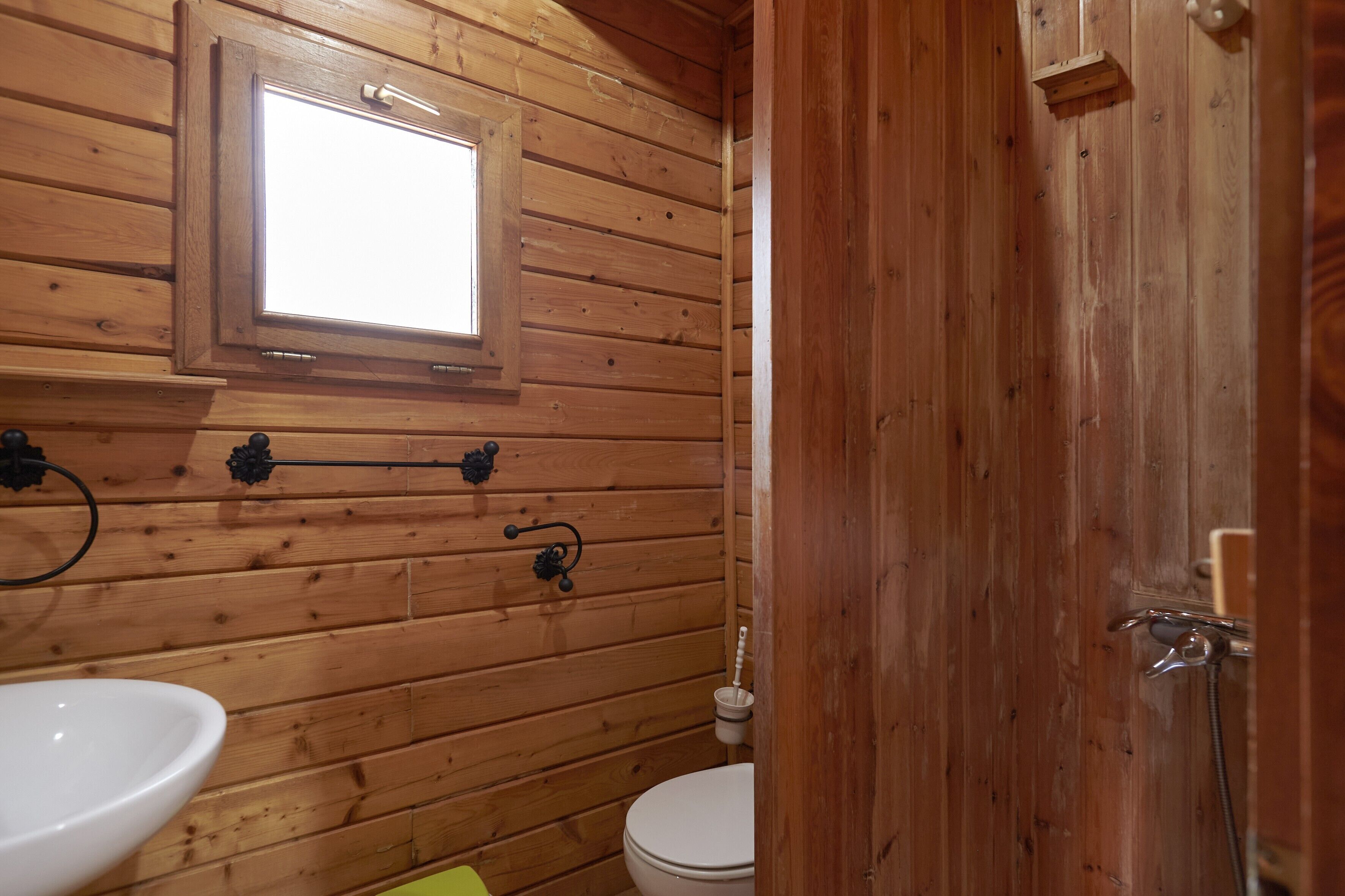 A wooden bathroom with a window, a toilet, and a sink.