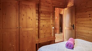 Een houten kamer met een bed, een houten kledingkast en een deur naar een andere ruimte.