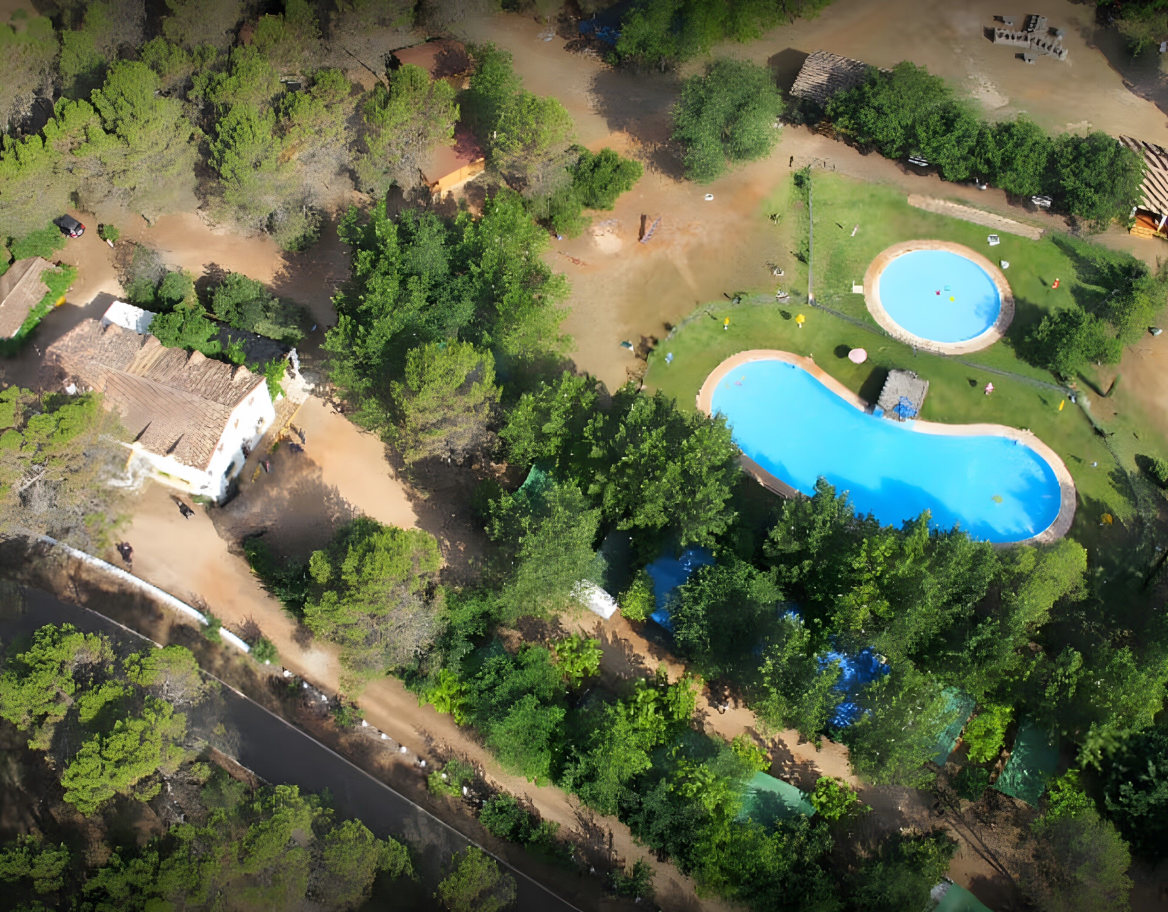 Vista aérea de una propiedad con dos piscinas, un edificio blanco y abundante vegetación.