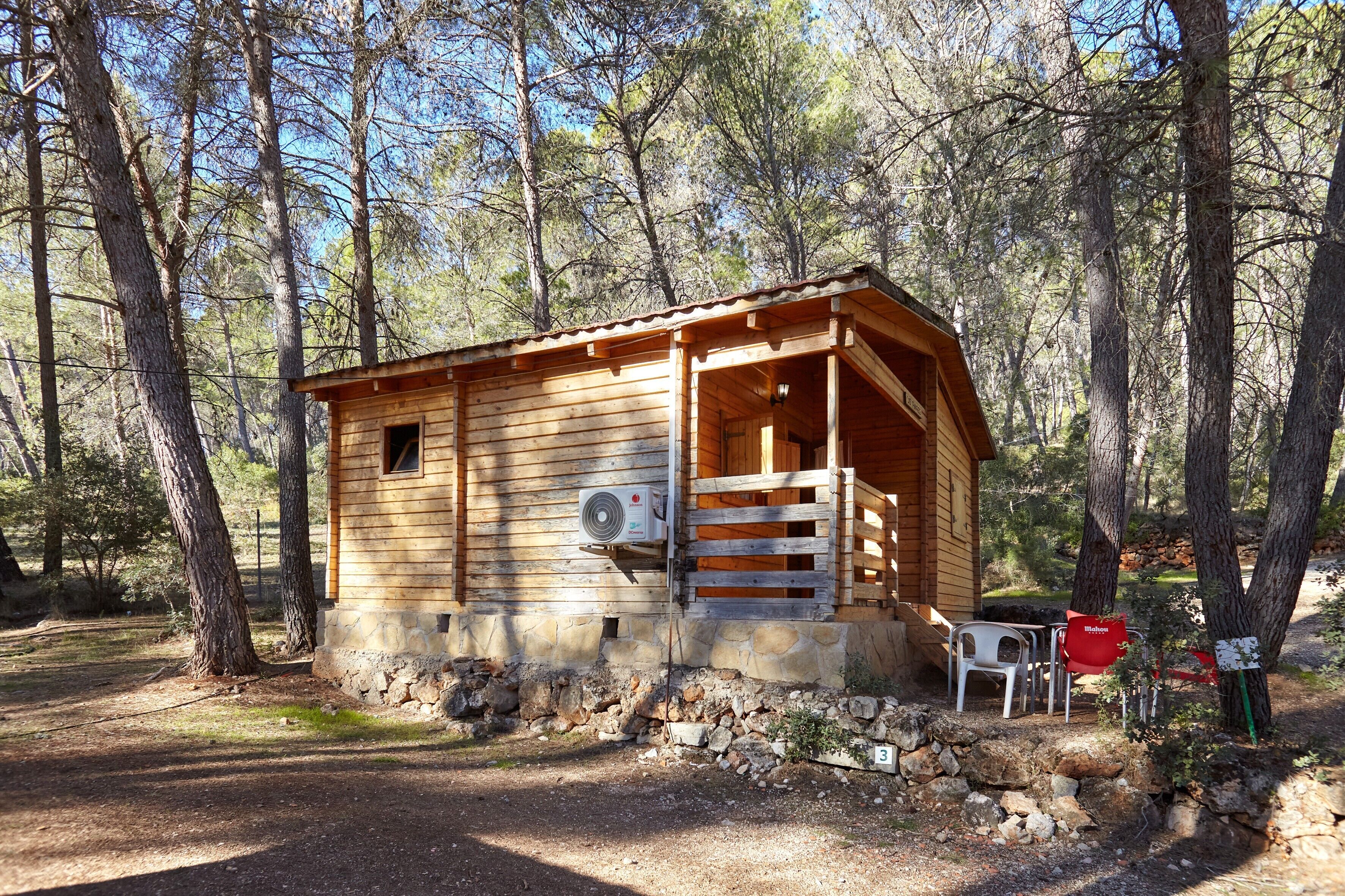 Une cabane en bois dotée d’un porche, de fondations en pierre et d’un petit espace extérieur aménagé pour s’asseoir.