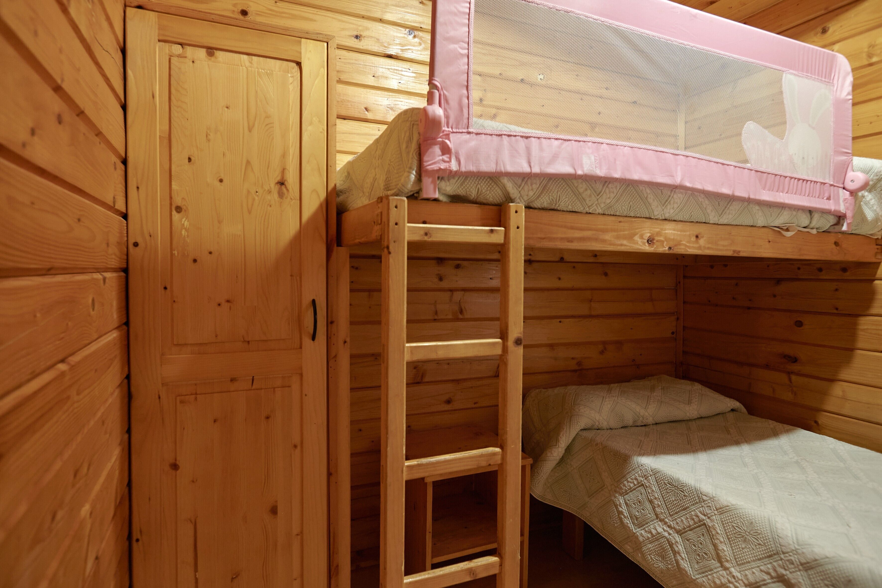 Een houten stapelbed met een ladder, een klein afgesloten slaapgedeelte en een houten kledingkast.