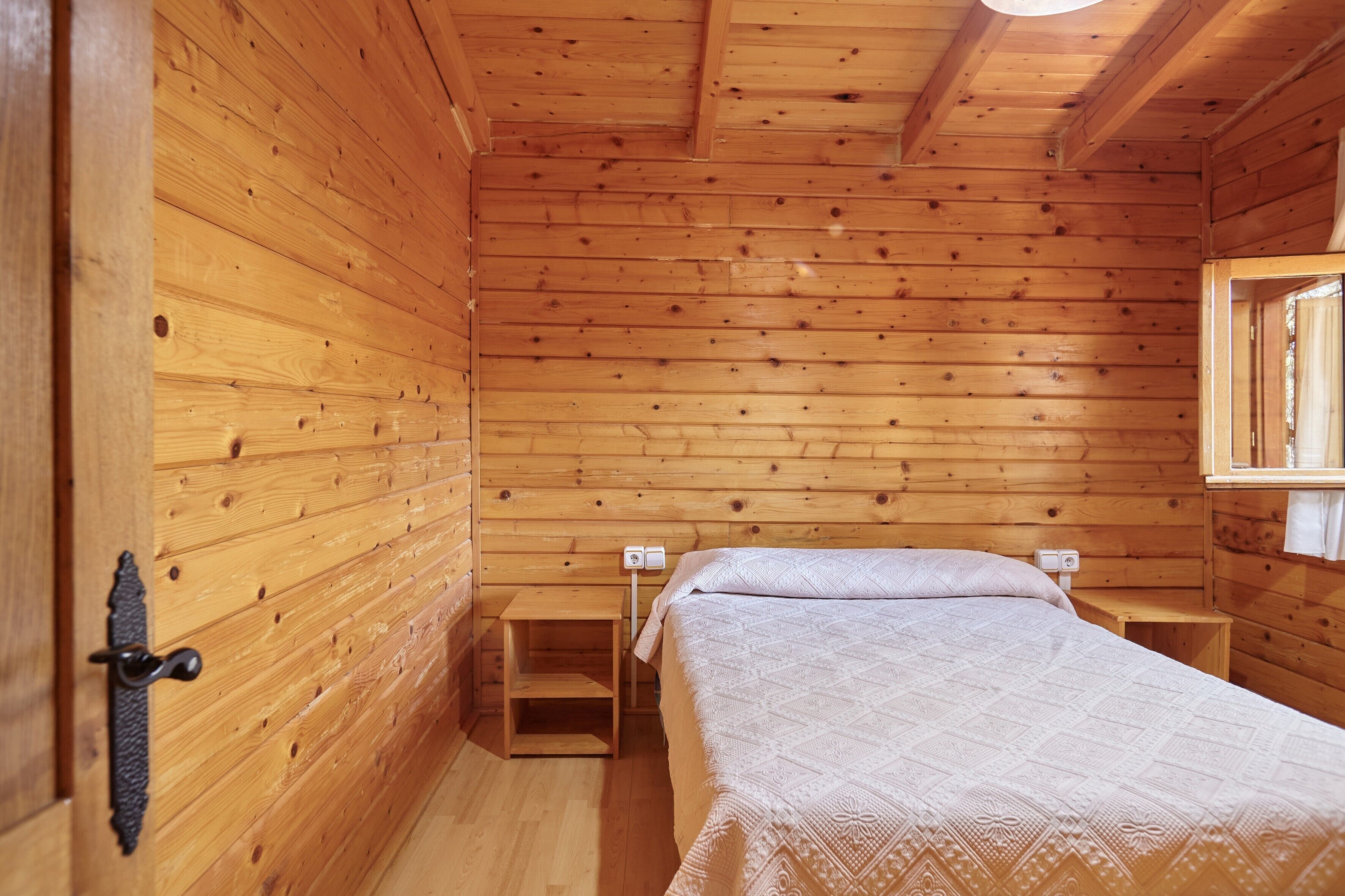 Un dormitorio de cabaña de madera con cama, mesitas de noche y una ventana.