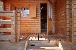 Eine Holzhütte mit einer Holzterrasse, einem Fenster mit Fensterläden und einer Tür.