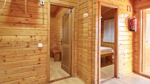 A wooden cabin interior with a bed, a bench, a fire extinguisher, and a power outlet.
