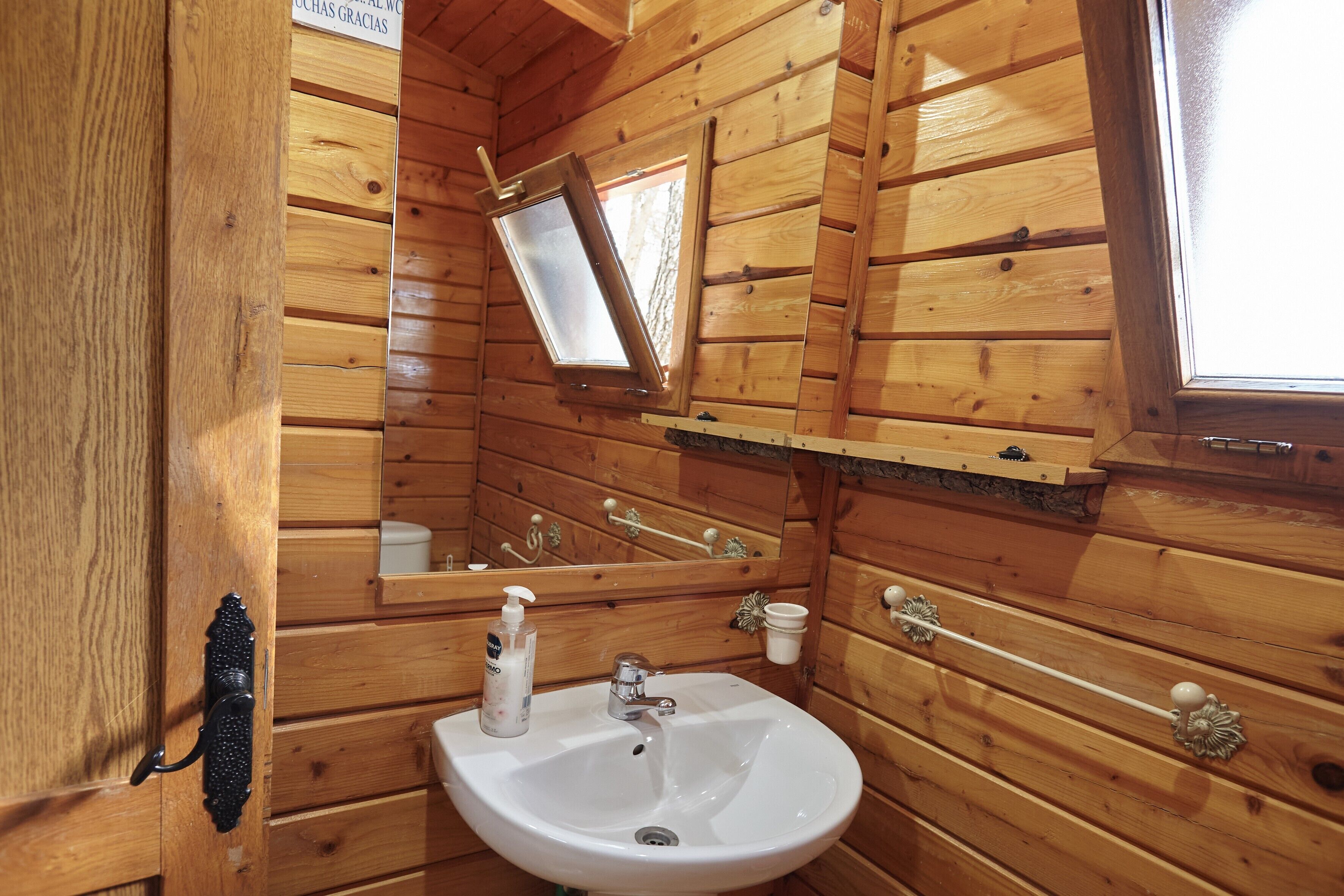 A wooden cabin bathroom with a sink, mirror, and window.