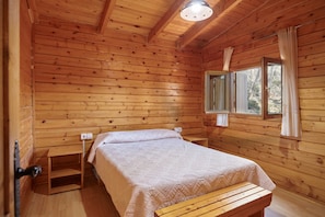 Ein Schlafzimmer einer Holzhütte mit einem Bett, einer Bank, einem Fenster mit Vorhängen und einer Deckenleuchte.