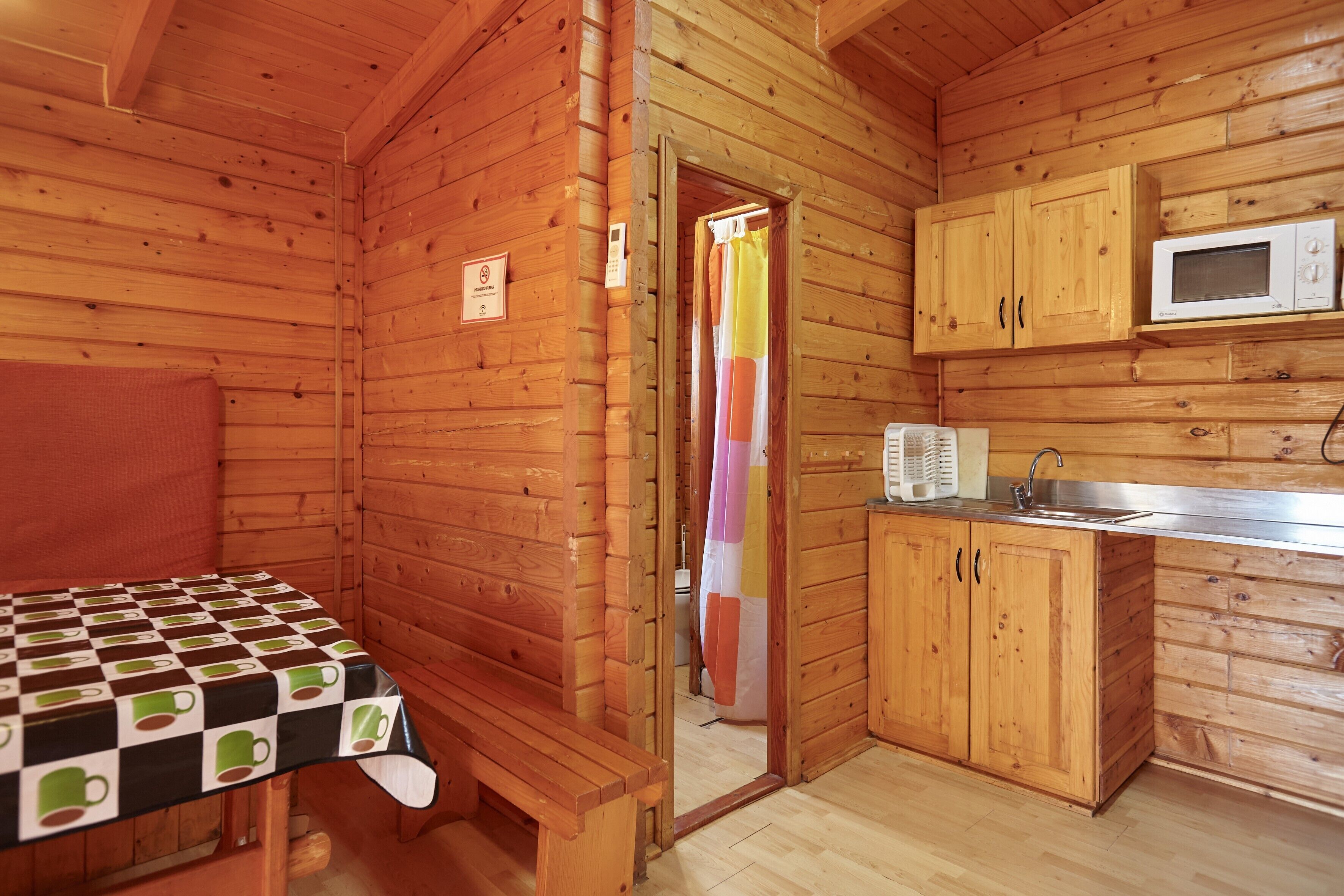 Una cabaña de madera con una mesa a cuadros, un banco, un microondas y armarios de madera.