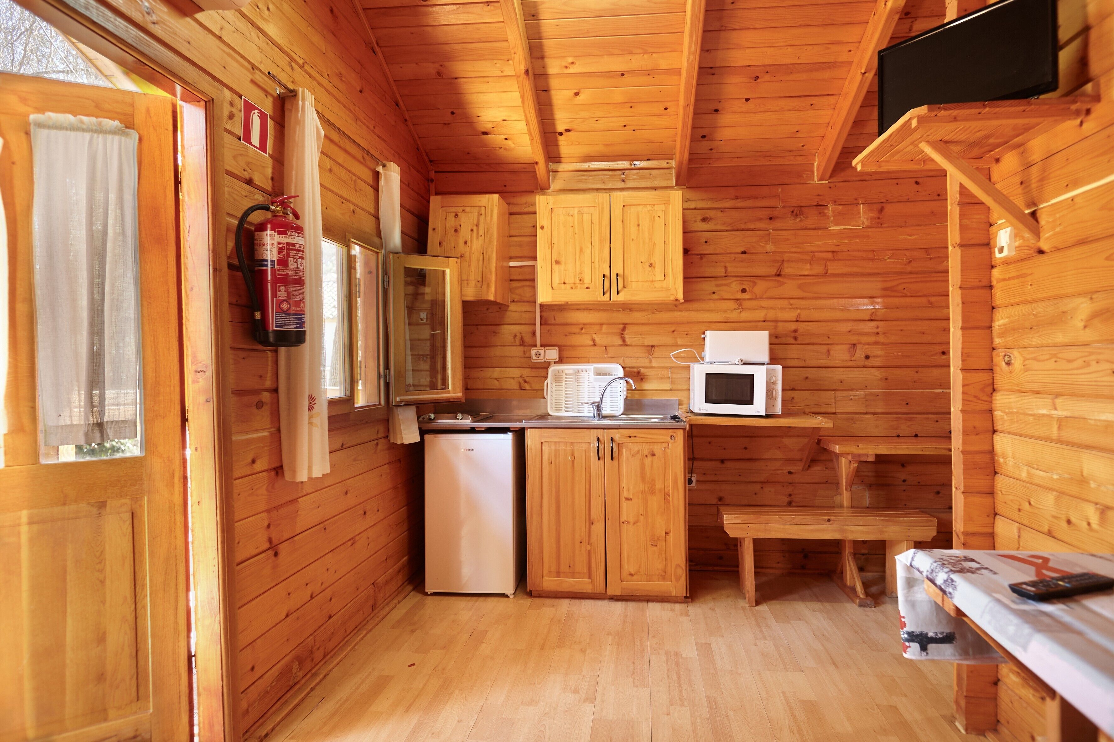 Interieur van een houten hutje met een kitchenette, een brandblusser, een magnetron en een eettafel.