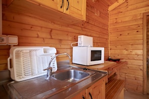 Ein Holzblockhaus-Innenraum mit einer Küchenzeile, die ein Spülbecken, eine weiße Mikrowelle und eine Kaffeemaschine enthält.